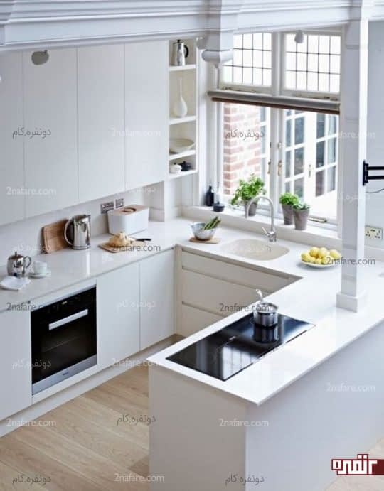 یک آشپزخانه سفید مینیمال با کابینت های براق و یک پنجره بزرگ برای پر کردن فضا با نور