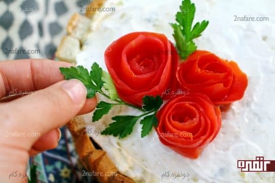 قرار دادن گل های رز گوجه ای و قرار دادن برگ های جعفری روی کیک